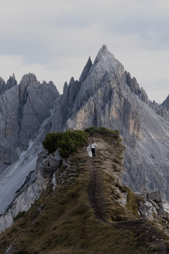 Person standing on a narrow mountain ridge beneath jagged peaks